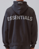 mężczyzna w czarnej bluzie essentials stojący tyłem do zdjęcia i prezentujący logo essentials na bluzie